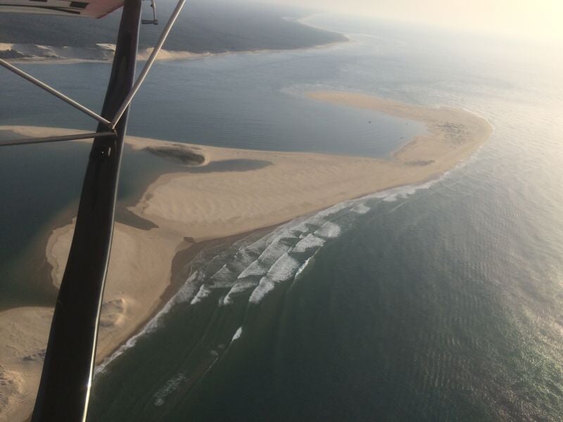 Vue aérienne d'une plage de sable et dunes avec vagues, prise depuis un avion ultraléger motorisé.