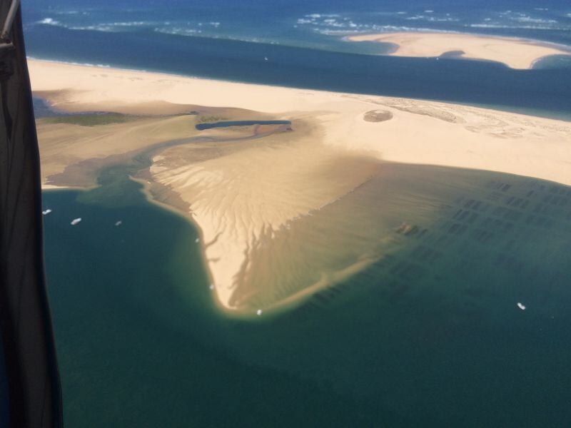 Vue aérienne d'une grande dune de sable entourée d'eau prise depuis un avion ultraléger motorisé.