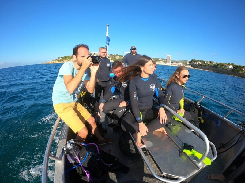 Groupe de personnes en combinaison de plongée sur un bateau en mer, avec un photographe prenant des photos.