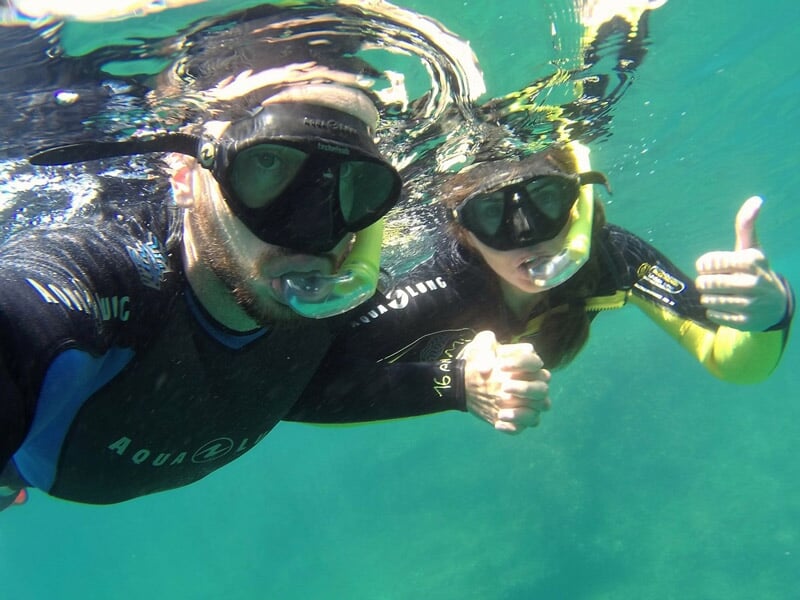 Deux plongeurs sous-marins en combinaison noire avec masque, nageant sous l'eau et faisant un pouce levé.