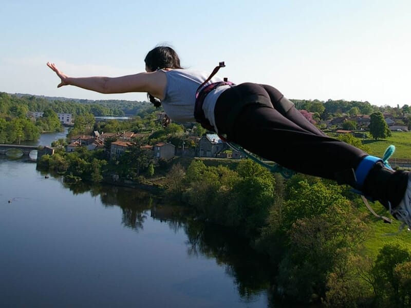 Personne en train de faire un saut à l'élastique au-dessus d'une rivière avec un paysage verdoyant en arrière-plan.