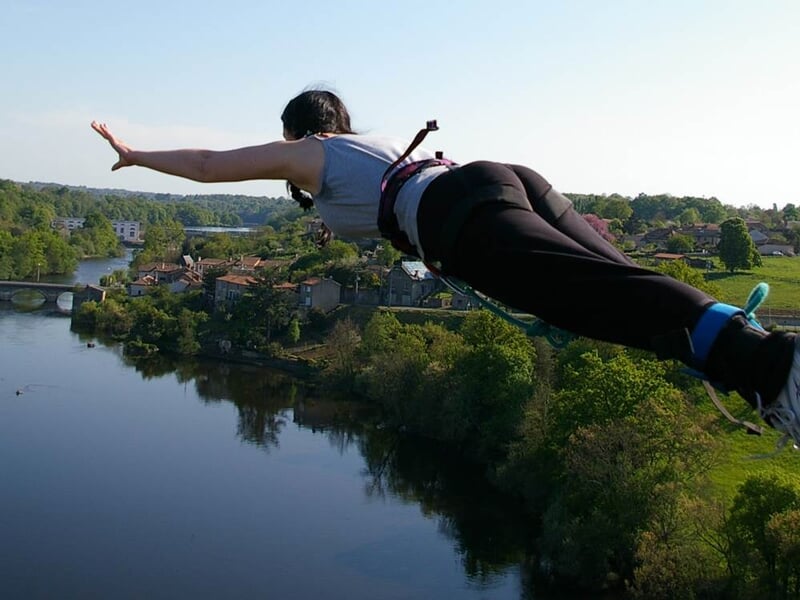 Personne en train de faire un saut à l'élastique au-dessus d'une rivière avec un paysage verdoyant en arrière-plan.