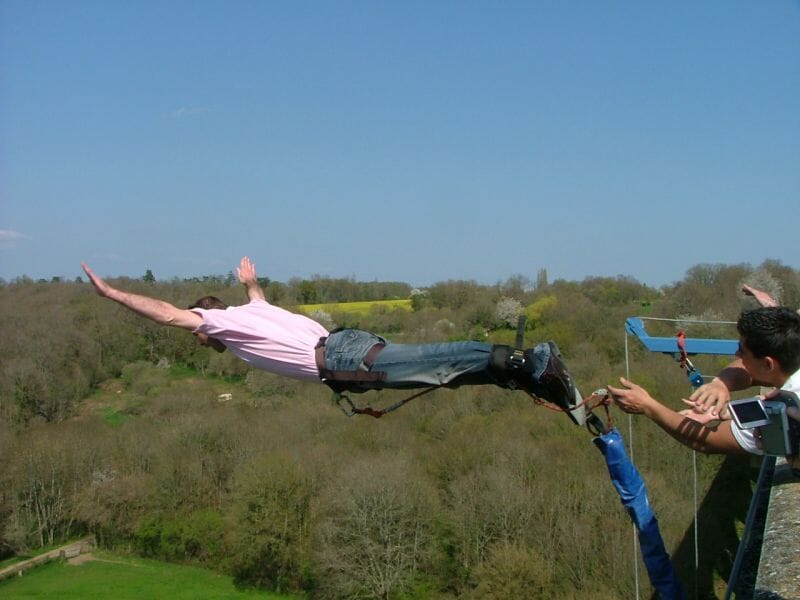 Personne en train de faire un saut à l'élastique depuis un pont, bras tendus, paysage de forêt en arrière-plan