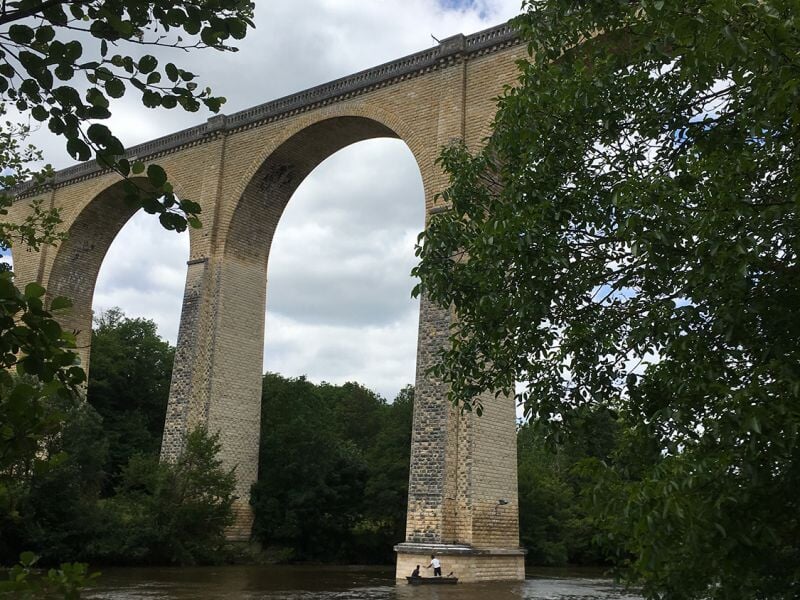 Viaduc du Blanc en pierre avec arches imposantes au-dessus d'une rivière, entouré d'arbres verts sous un ciel nuageux.