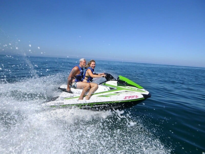 Un homme et une femme sur un jetski vert et blanc glissant rapidement sur l'eau avec des éclaboussures.