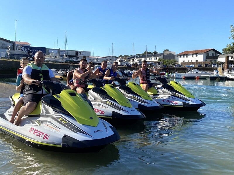 Groupe de six personnes posant sur plusieurs jetskis alignés dans un port avec des bâtiments en arrière-plan.