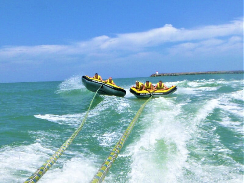 Deux grosses bouées tractées jaunes sur l'eau, tirées par un bateau, avec des passagers portant des gilets.
