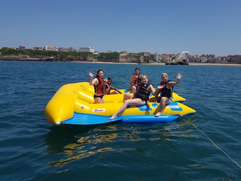 Quatre personnes souriantes assises sur une grande bouée jaune et bleue flottant sur l'eau.