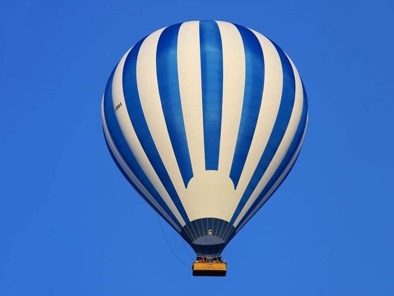 Montgolfière à rayures verticales bleues et blanches en vol, contrastant avec le ciel bleu intense