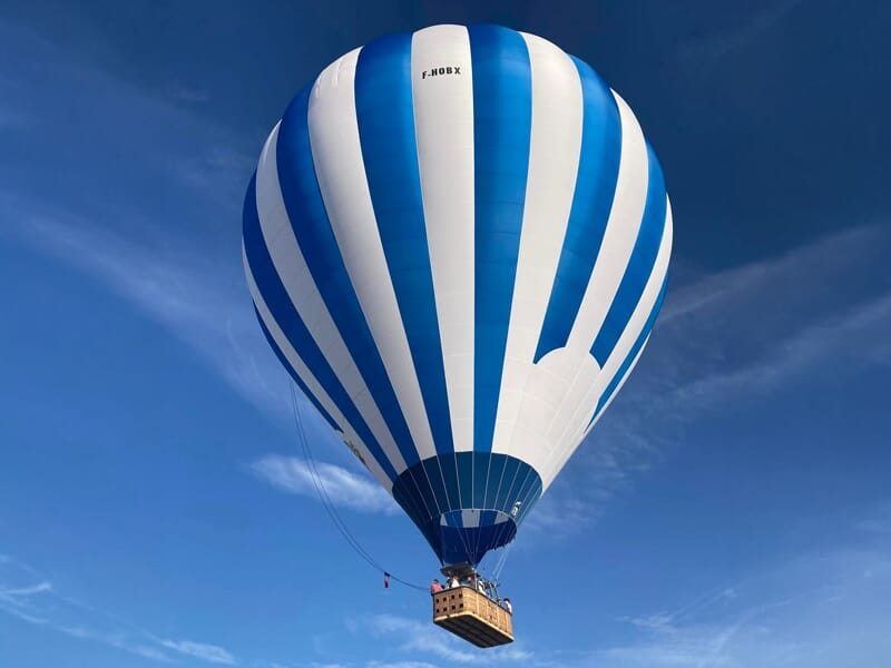 Gros plan d'une montgolfière bleue et blanche avec une nacelle suspendue, sur fond de ciel bleu clair.