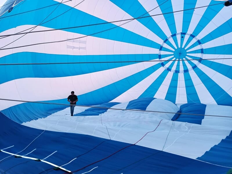 Personne debout à l'intérieur d'une montgolfière bleue et blanche en cours de gonflage, vue de l'intérieur.