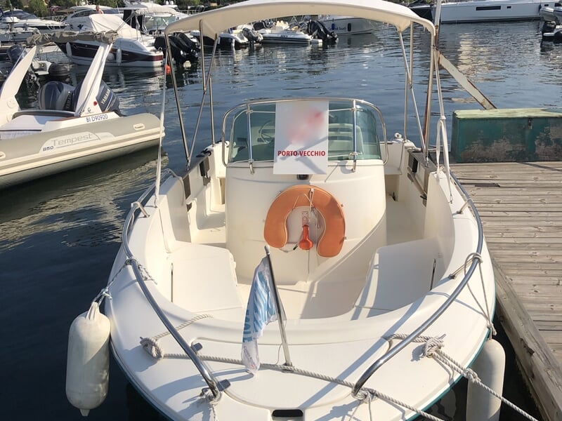 Bateau école blanc amarré au quai avec bouée orange et drapeau bleu, entouré d'autres bateaux au port.