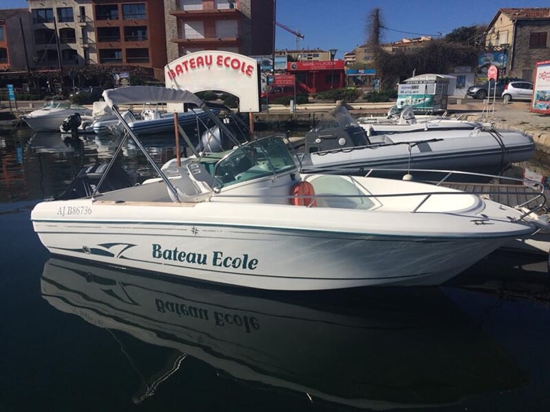 Bateau école blanc avec inscription sur la coque, amarré dans un port urbain avec bâtiments en arrière-plan.