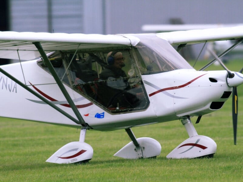 Petit avion ultraléger blanc avec des motifs rouges, stationné sur une pelouse verte.