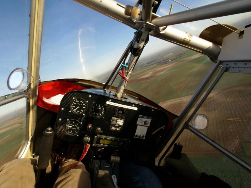 Vue depuis le cockpit d'un ULM en vol, montrant les instruments de bord et le paysage agricole en dessous.