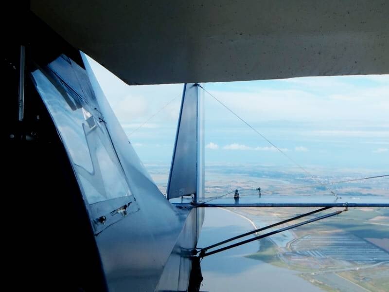 Vue depuis l'arrière d'un avion ultraléger en vol, montrant l'aile et le paysage côtier en dessous.
