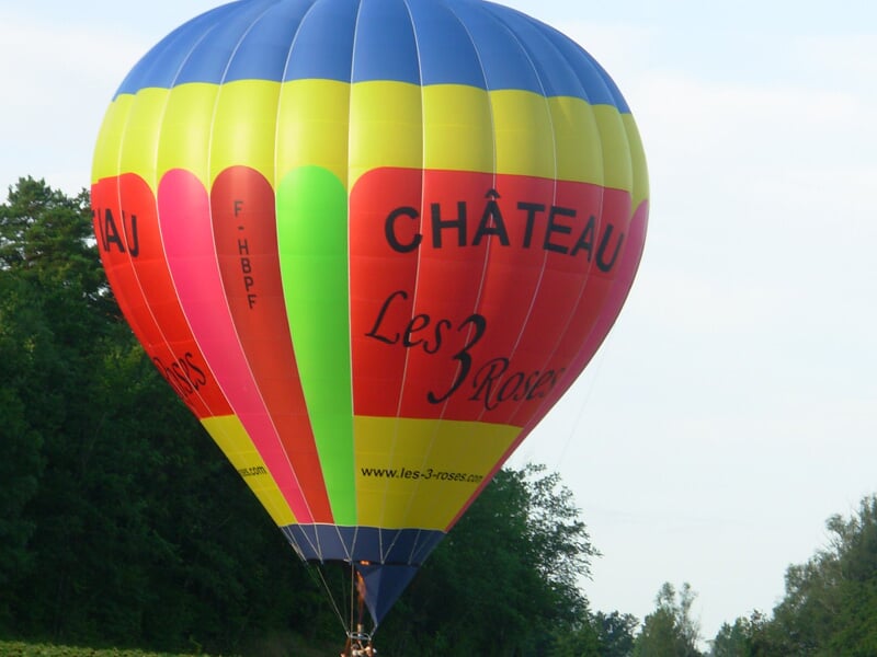 Gros plan sur une montgolfière aux couleurs vives jaune, rouge et bleu avec l'inscription Château Les 3 Roses.