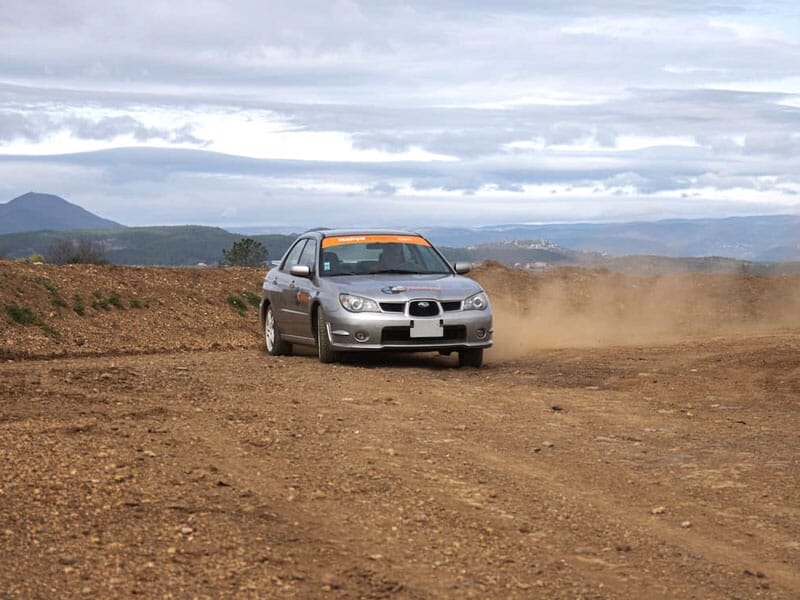 Subaru grise effectuant un virage rapide sur une piste de rallye en terre, laissant une traînée de poussière derrière elle