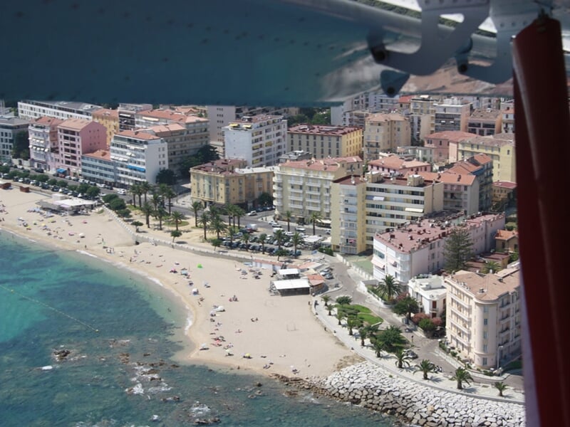 Plage urbaine avec sable clair, baigneurs et immeubles en arrière-plan sous un ciel bleu clair