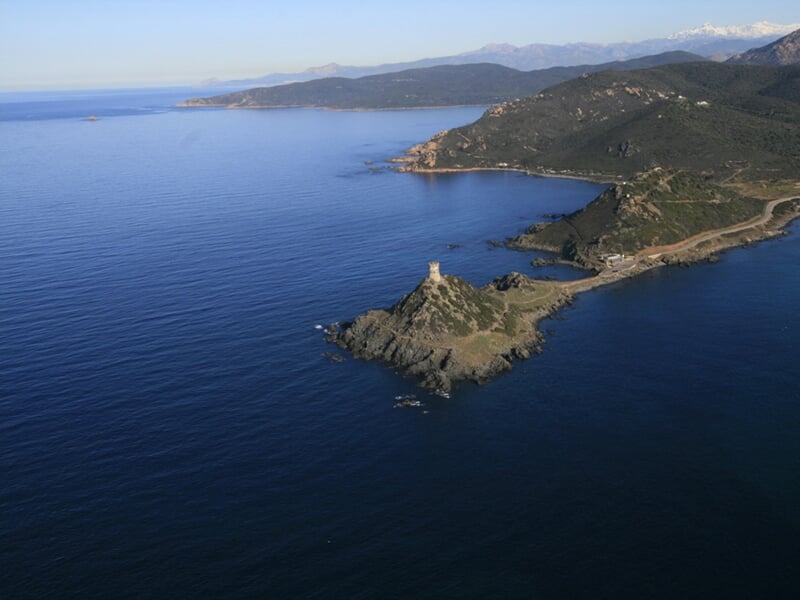 Paysage côtier avec une tour ancienne sur une pointe rocheuse entourée par la mer calme