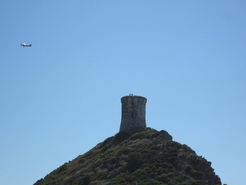 Tour génoise sur une colline avec un petit avion volant à proximité dans un ciel bleu sans nuages