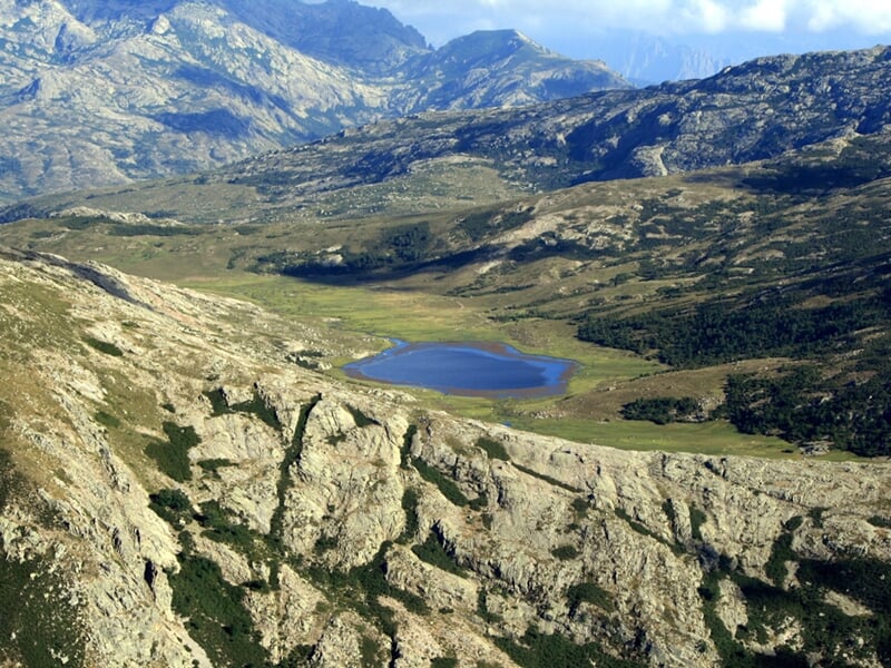 Paysage montagneux avec un lac d'altitude entouré de rochers et de végétation sous un ciel clair