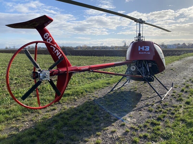 hélicoptère ULM vu de dos, posé au milieu d'un pré