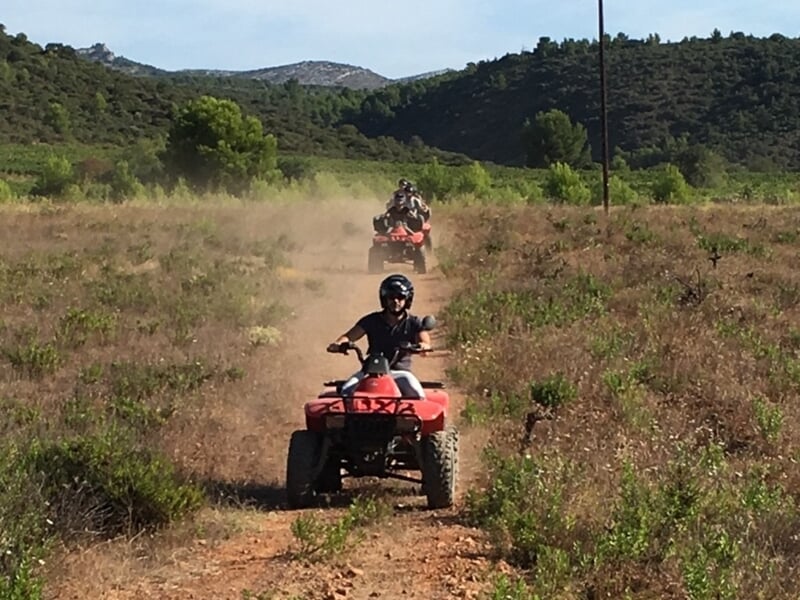 Personnes en quad rouge roulant sur un chemin poussiéreux dans un paysage de collines et végétation verte.