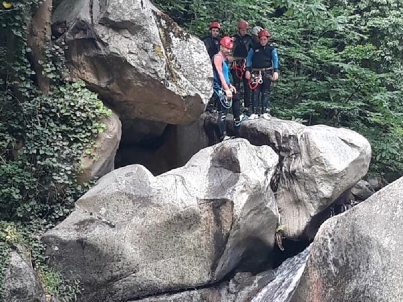 Groupe de personnes équipées de casques et combinaisons prêtes pour une activité de canyoning près de gros rochers.