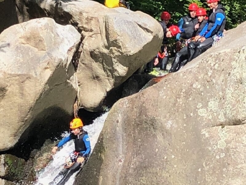 Personne en combinaison et casque jaune glissant sur un rocher mouillé lors d'une descente de canyoning en rivière.