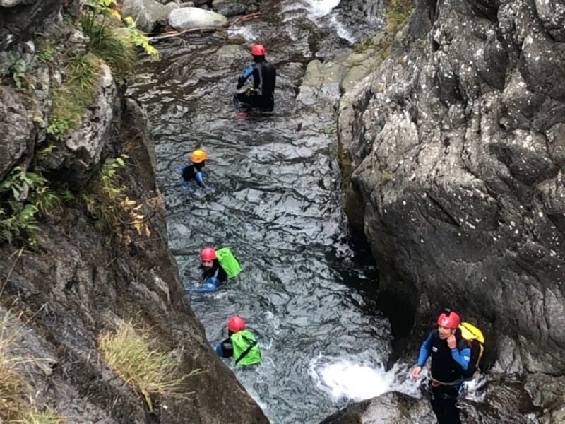 Groupe de personnes en combinaisons et casques rouges nageant et marchant dans une rivière encaissée pour canyoning.