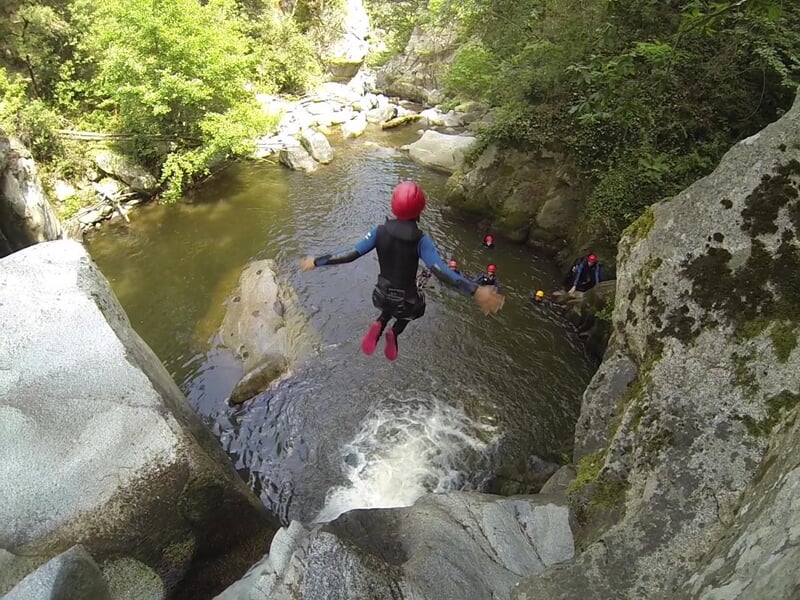 Personne sautant dans l'eau depuis un rocher lors d'une activité de canyoning en rivière entourée de végétation.