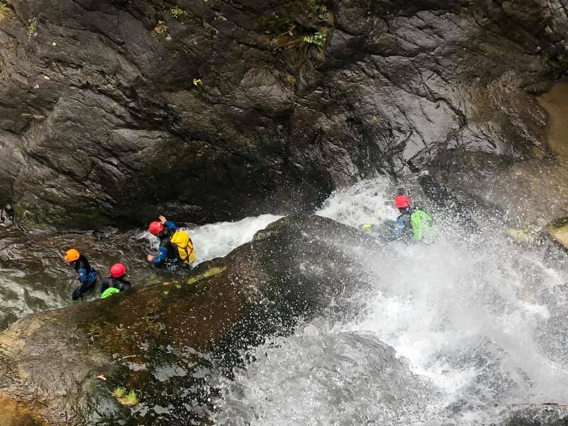 Groupe de personnes en combinaisons de canyoning descendant une cascade d'eau avec éclaboussures dans un canyon rocheux.