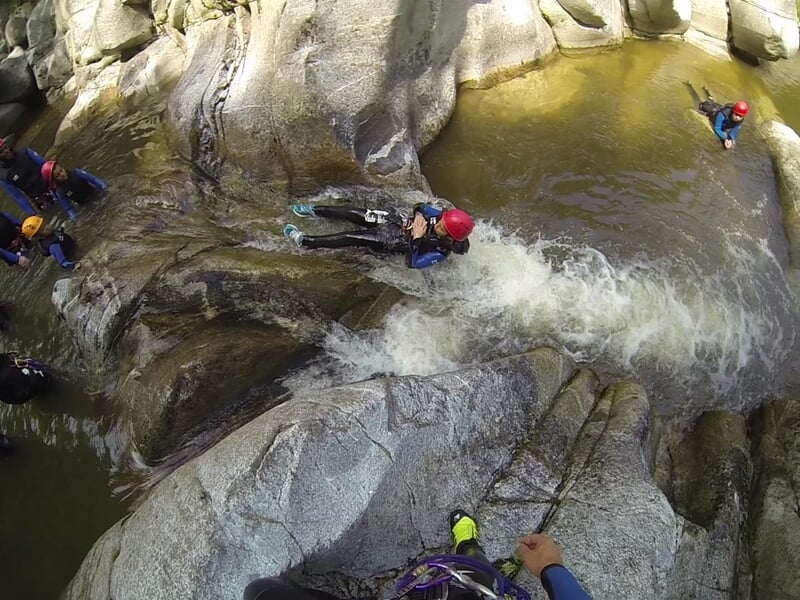 Vue plongeante sur des personnes en combinaisons de canyoning descendant une cascade d'eau dans un canyon étroit.