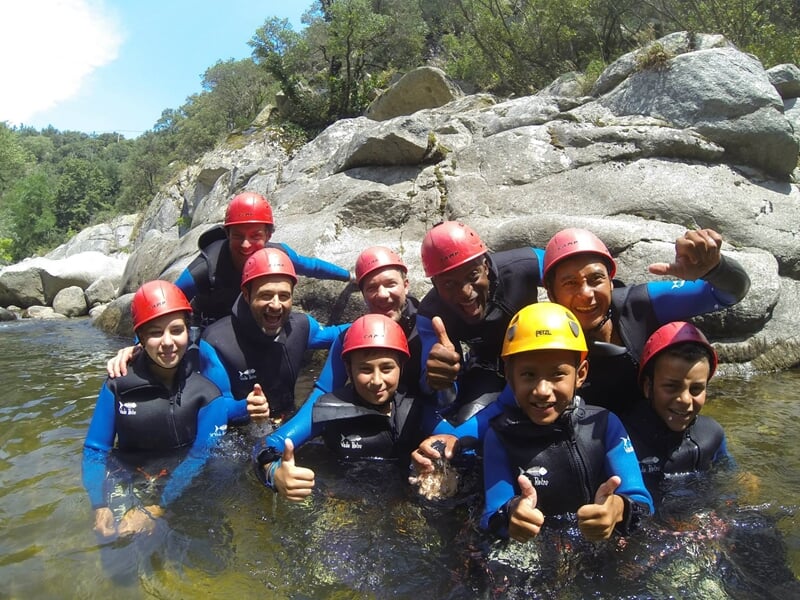 Groupe souriant en combinaisons et casques rouges posant dans l'eau d'une rivière lors d'une sortie canyoning.