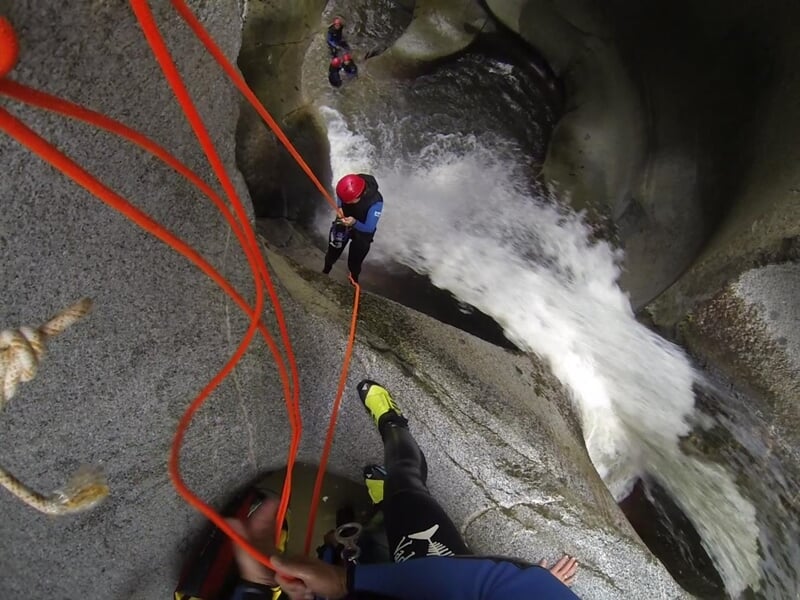 Personne descendant en rappel le long d'une cascade d'eau dans un canyon rocheux lors d'une activité de canyoning.