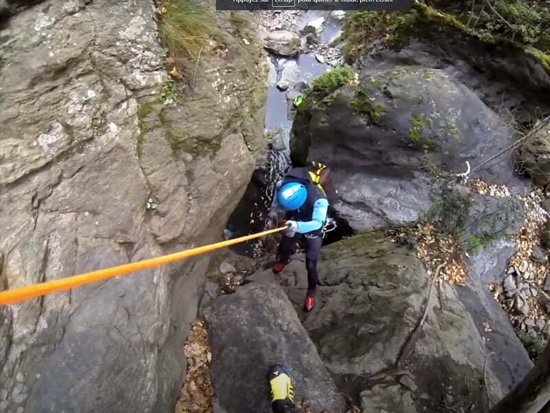Personne en combinaison bleue descendant en rappel le long d'une paroi rocheuse dans un canyon étroit.