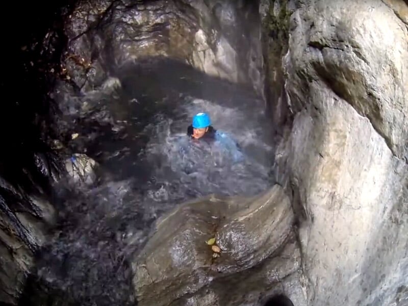 Personne en combinaison bleue nageant dans une rivière encaissée entourée de rochers lors d'une sortie canyoning.