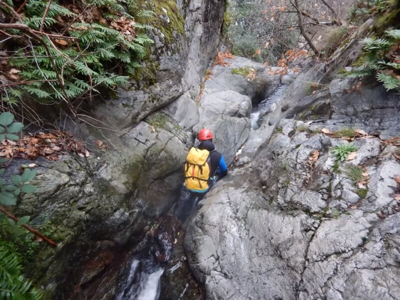 Personne en combinaison et casque rouge descendant une cascade d'eau dans un canyon rocheux étroit.