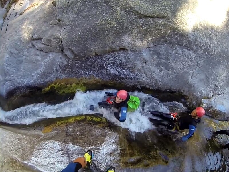 Personnes en combinaisons et casques rouges marchant dans un canyon rocheux étroit avec de l'eau et des rochers.