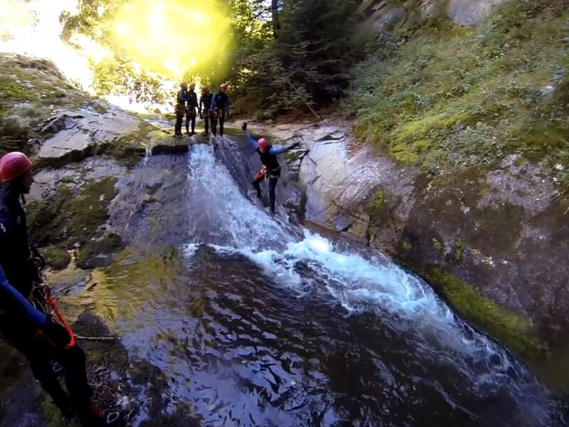 Personnes en combinaisons et casques rouges descendant une cascade d'eau dans un canyon étroit et rocheux.