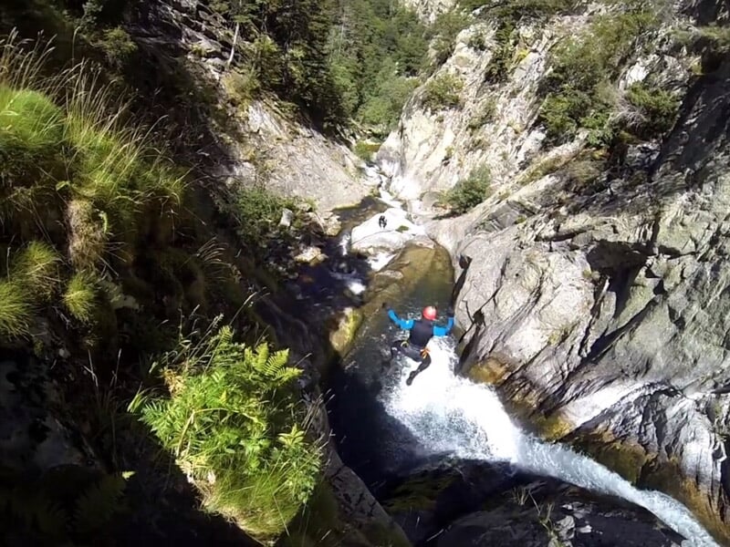 Personne en combinaison bleue descendant en rappel une cascade d'eau dans un canyon rocheux étroit et escarpé.