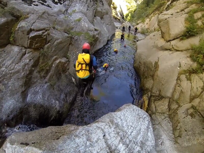 Personne en combinaison bleue descendant une cascade d'eau dans un canyon rocheux étroit avec de l'eau claire.