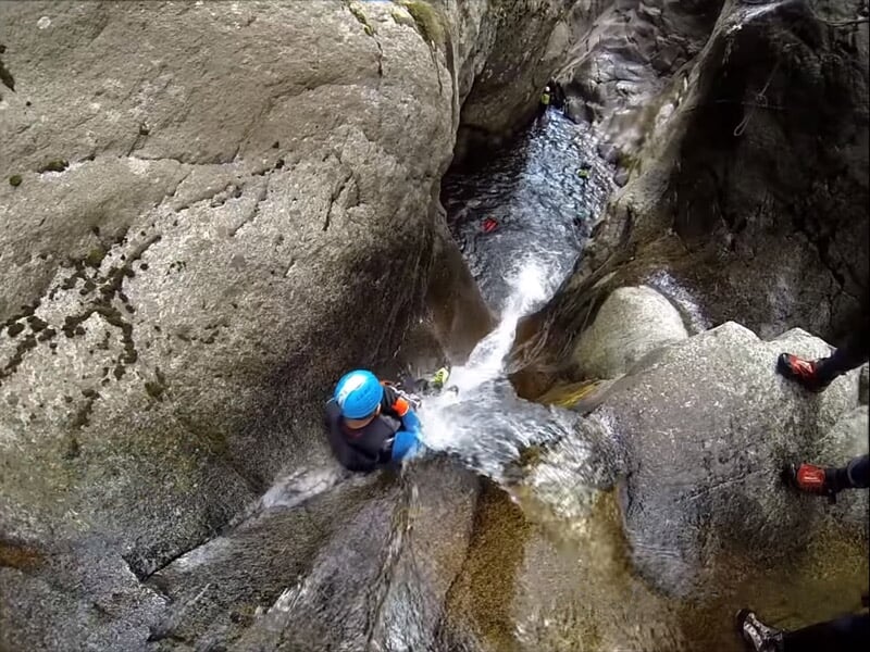 Personnes en combinaisons et casques rouges descendant une cascade d'eau dans un canyon étroit et rocheux.