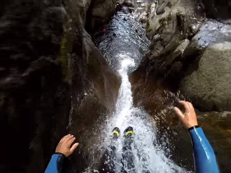 Personne en combinaison bleue descendant en rappel une cascade d'eau dans un canyon rocheux étroit et escarpé.