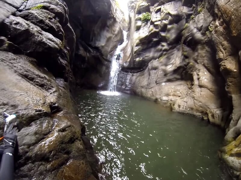 Personne en combinaison bleue descendant une cascade d'eau dans un canyon rocheux étroit avec de l'eau claire.