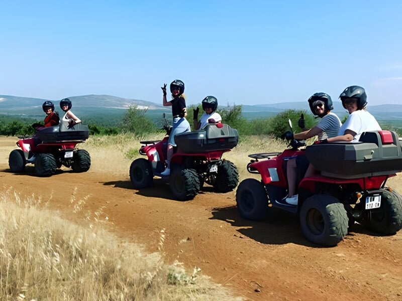 Groupe de personnes en quad rouge roulant sur un chemin de terre dans un paysage de campagne avec ciel bleu.