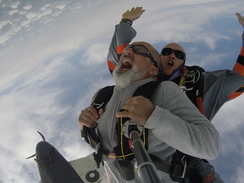 Personne en parachute en chute libre au-dessus d'un paysage vert avec arbres et champs.