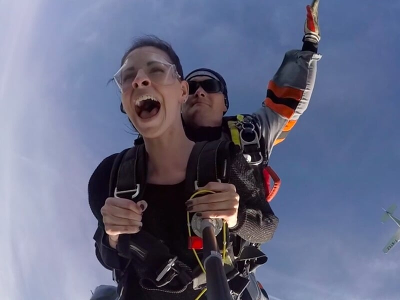Saut en parachute tandem, deux personnes en chute libre avec paysage naturel en arrière-plan.
