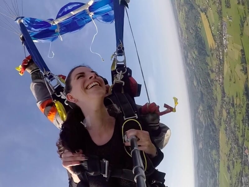 Parachutiste en tandem en chute libre, bras écartés avec paysage naturel en arrière-plan.